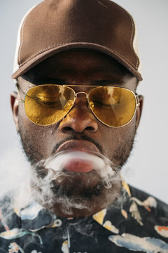 Black stylish man wearing sunglasses. He is vaping with an electronic cigarrete outdoor