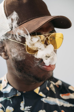 Black stylish man wearing sunglasses. He is vaping with an electronic cigarrete outdoor