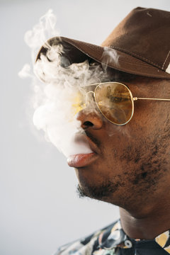 Black stylish man wearing sunglasses. He is vaping with an electronic cigarrete outdoor