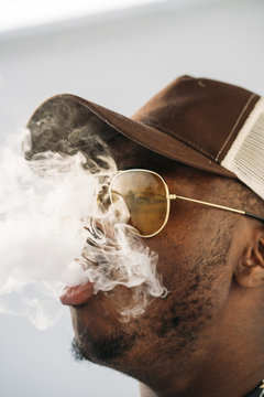 Black stylish man wearing sunglasses. He is vaping with an electronic cigarrete outdoor