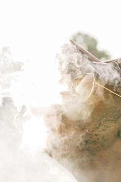 Black stylish man wearing sunglasses. He is vaping with an electronic cigarrete outdoor