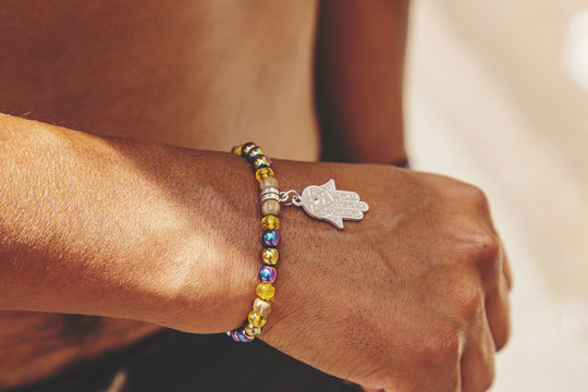 Male hand wrist with colorful bracelet and hamsa silver pendant