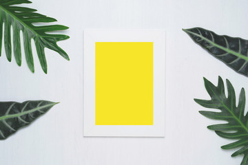 Stylish minimal composition with white photo frame and green leaves on a white wooden background. Empty photo frame and green leaves. flat lay, top view.