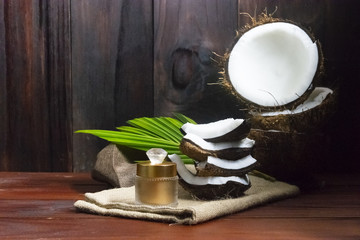 Face cream coconut oil and coconut half with coconut pieces and leaf on wooden background.
