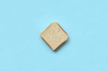 A piece of bread lies on texture background of fashion pastel blue color paper in minimal concept