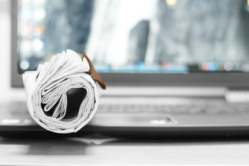 Computer and newspapers. Rolled papers with news on keyboard of laptop. Different sources of...