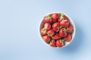 Ripe strawberry in bowl top view on blue background
