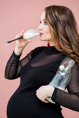 Beautiful young pregnant woman drink milk in a champagne glass. Pregnant woman celebrating her pregnancy