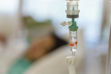 Saline solution for intravenous infusion in hospital, infusion dripping drops. Slow treatment with blur woman patient . selective focus.