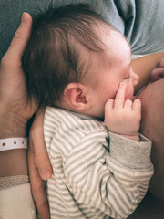 cute newborn baby showing middle finger while drinking milk from mother's breast