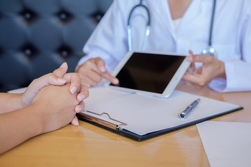 Patient listening intently to a male doctor explaining patient symptoms or asking a question as they discuss paperwork together in a consultation