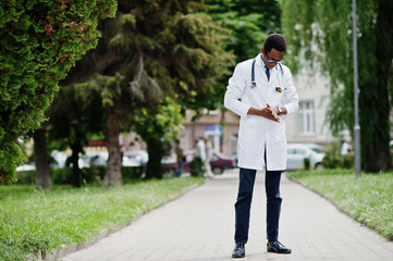 Stylish african american doctor with stethoscope and lab coat, at glasses posed outdoor.