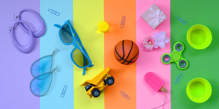 Trendy pastel composition with earrings, sunglasses, beverage can, basketball ball, toy truck, gift box, ice cream, flower and spinner on pink, violet, green, orange, yellow and blue colors