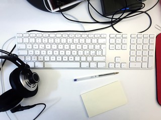 top view of a computer keyboard with a pen, a memo and headphones