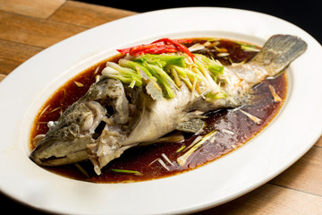 Steamed snapper with soy sauce in white dish on wood table.