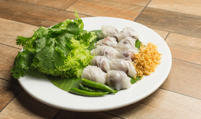 Thai steamed rice-skin dumpling with deep fried garlic and chilli in white dish on wood table.