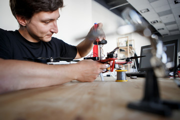 Image of man with screwdriver fixing square copter at table