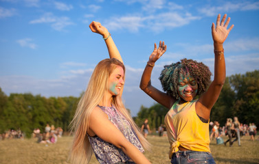 Two multiethnic girls covered in colorful powder dancing and celebrating summer holi festival