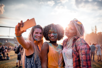 Multiethnic girls covered in colorful powder taking selfie at summer holi festival