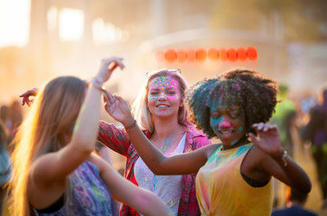 Multiethnic girls covered in colorful powder celebrating summer holi festival