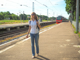 Lady traveler with backpack on back on the railway platform in a small European city.