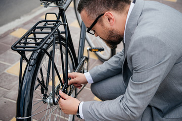 Fototapeta na wymiar handsome bearded businessman in grey suit repairing bicycle wheel