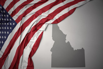 waving national flag of united states of america on a gray idaho state map background.