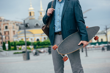 cropped view of man with leather bag and longboard walking in city
