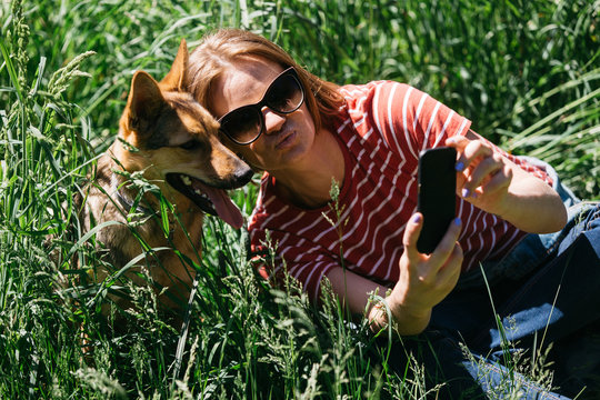 Photo of woman doing selfie on walk with dog on green lawn