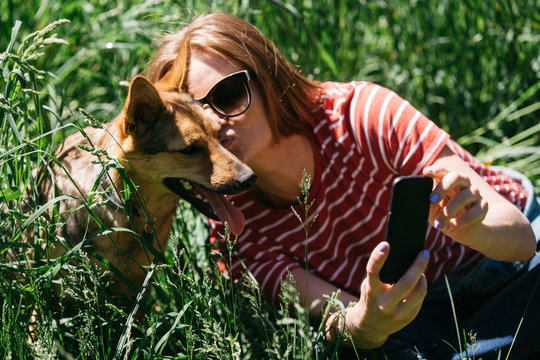 Image of woman doing selfie on walk with dog on green lawn