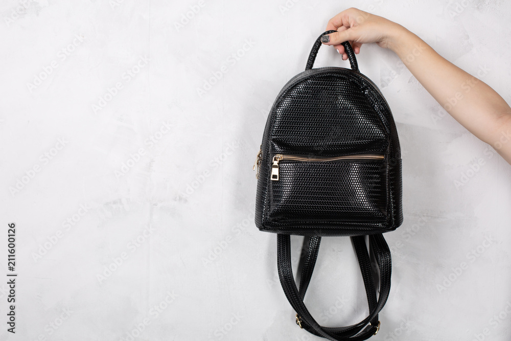 Wall mural female hand holding small leather backpack against white wall. empty space