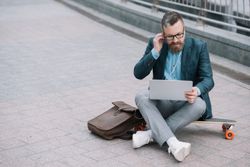 bearded man using laptop with earphones and sitting on skateboard in city © LIGHTFIELD STUDIOS