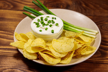 Crispy potato chips with green onion and sour cream on wooden table