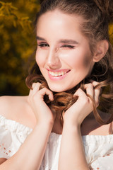 Closeup portrait of cheerful winking woman with curly hair standing near yellow blooming flowers