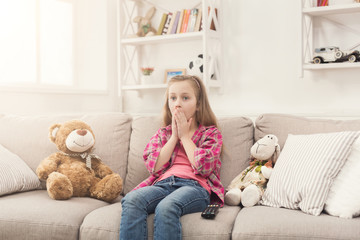 Shocked little girl watching tv sitting on sofa