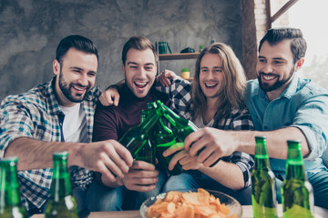 Four attractive, stylish, confident, successful, bearded guys with modern hairstyle, embracing, clinking bottle with lager for goal, unity spending time together in livingroom
