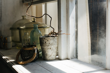 Dry plant in a vase and a glass capacity on a windowsill in a large wooden window. Empty space
