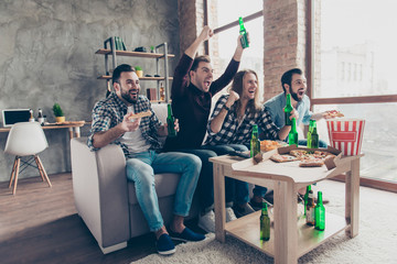 Four stylish, successful, attractive guys with raised arms, cheer for favorite team, watching football, basketball match together, yelling, drinking lager eating snacks, chips, popcorn, pizza