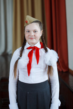 A modern girl with a red pioneer tie in a white shirt and a soldier's cap with a red star at a solemn meeting in honor of the Great Victory Day.