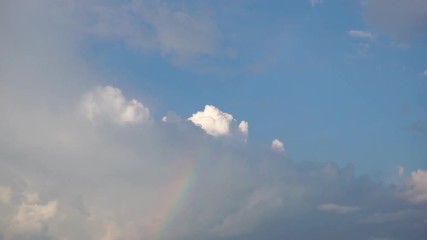 Rainbow under rain clouds against blue sky