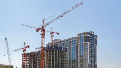 Construction cranes near buildings against blue sky. Construction site.