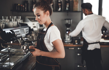 Fototapeta na wymiar Young woman barista preparing coffee using machine in the cafe