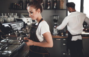 Young woman barista preparing coffee using machine in the cafe