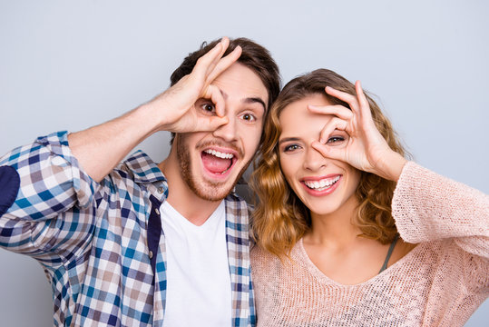Head shot portrait of funky cheerful couple gesturing ok sign around one eye keeping mouth open isolated on grey background