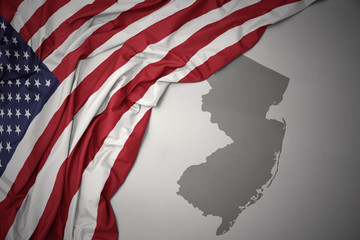 waving national flag of united states of america on a gray new jersey state map background.