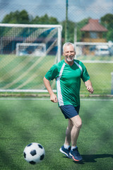 cheerful old man playing football on field on summer day