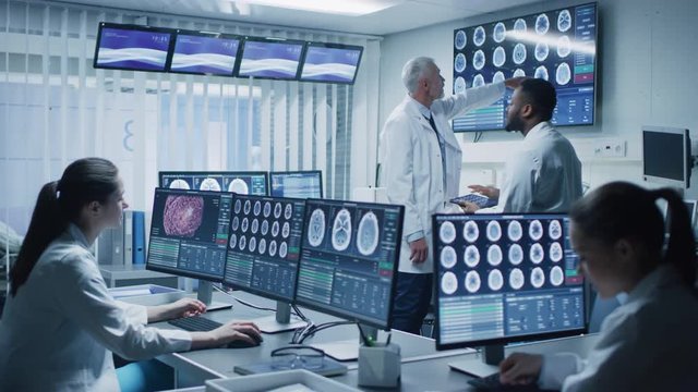 Team of Professional Scientists Work in the Brain Research Laboratory. Neurologists / Neuroscientists Surrounded by Monitors Showing CT, MRI Scans Having Discussions. Shot on RED EPIC-W 8K.