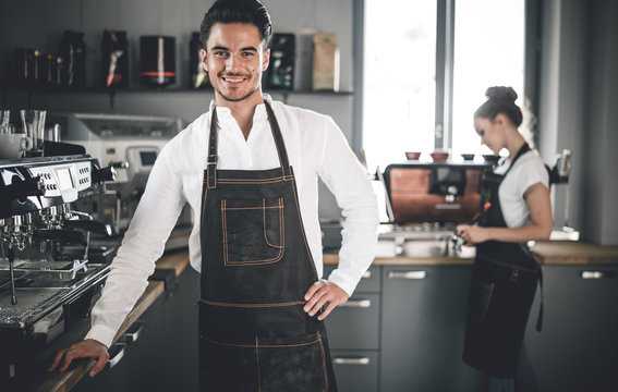 Professional barista in apron standing near coffee machines at cafe
