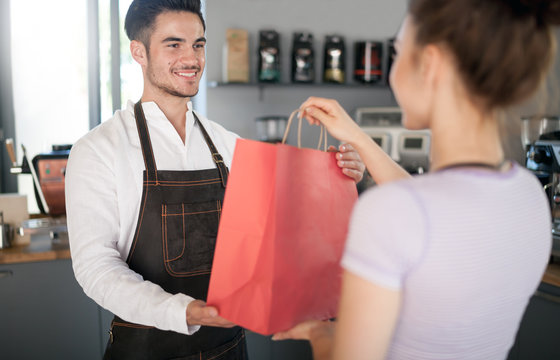 Professional barista giving shopping bag to customer at coffee shop, cafe small business