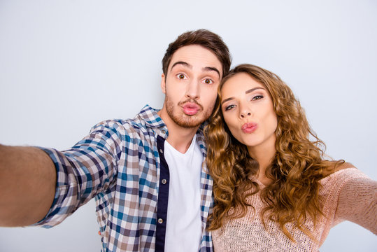 Self portrait of funny comic couple shooting selfie on front camera sending kiss with pout lips having online meeting isolated on grey background. Photography concept